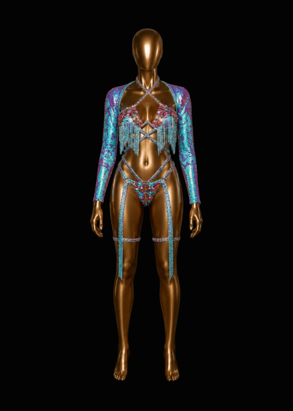 A metallic gold mannequin displays a highly embellished, iridescent two-piece costume with a long-sleeve crop jacket and matching bikini-style bottom, decorated with turquoise, pink, and blue sequins and fringe, set against a solid black background.