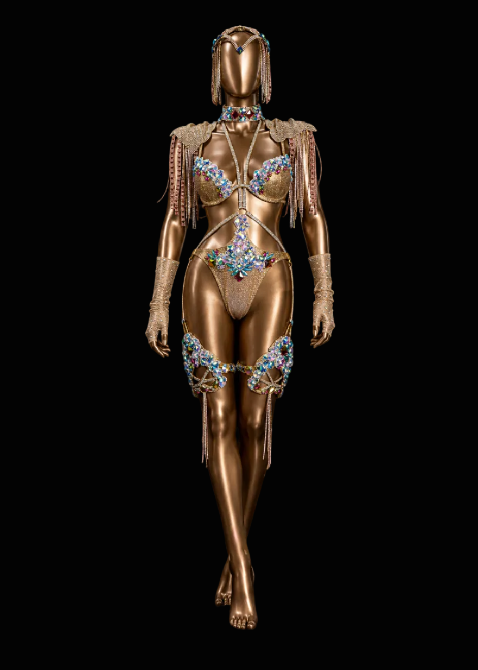 A metallic gold mannequin wearing an ornate, embellished belly dance costume with blue and turquoise rhinestones, set against a solid black background.
